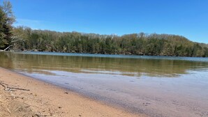 Una playa arenosa con un lago tranquilo y un cerro cubierto de bosque al fondo.