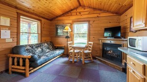 A cozy cabin interior with a sofa, dining table, chairs, a fireplace, a television, and a microwave. - Perfect for Couples, Pet Friendly, Bear Theme, Log Cabin, Fireplace (Mountain)