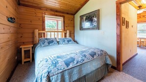 A wooden cabin room with a bed, a small table, a window, and a door leading outside. - Perfect for Couples, Pet Friendly, Bear Theme, Log Cabin, Fireplace (Mountain)
