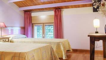 Ein Schlafzimmer mit zwei Betten, Holzbalkendecke, einem Fenster mit Vorhängen, einem Nachttisch mit Lampe und einem kleinen Tisch ebenfalls mit Lampe.