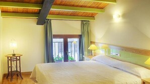 Una camera d'albergo con un letto, due lampade sui comodini, una finestra con tende e un soffitto in legno.