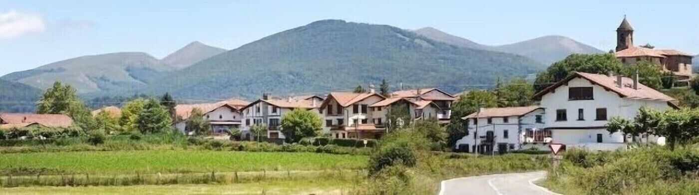 Un pueblo rural con casas, una carretera serpenteante y montañas al fondo.