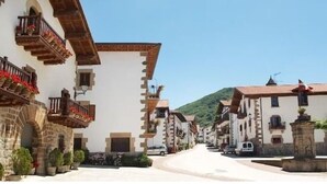 Una stretta via fiancheggiata da edifici tradizionali, alcuni con balconi e fioriere, che conduce a una collina.