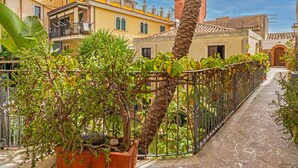 A courtyard with a palm tree, potted plants, a metal fence, and buildings with balconies and windows. - Apartment 'Casa Fabrizio' with Shared Terrace, Wi-Fi, and Air Conditioning (Taormina)