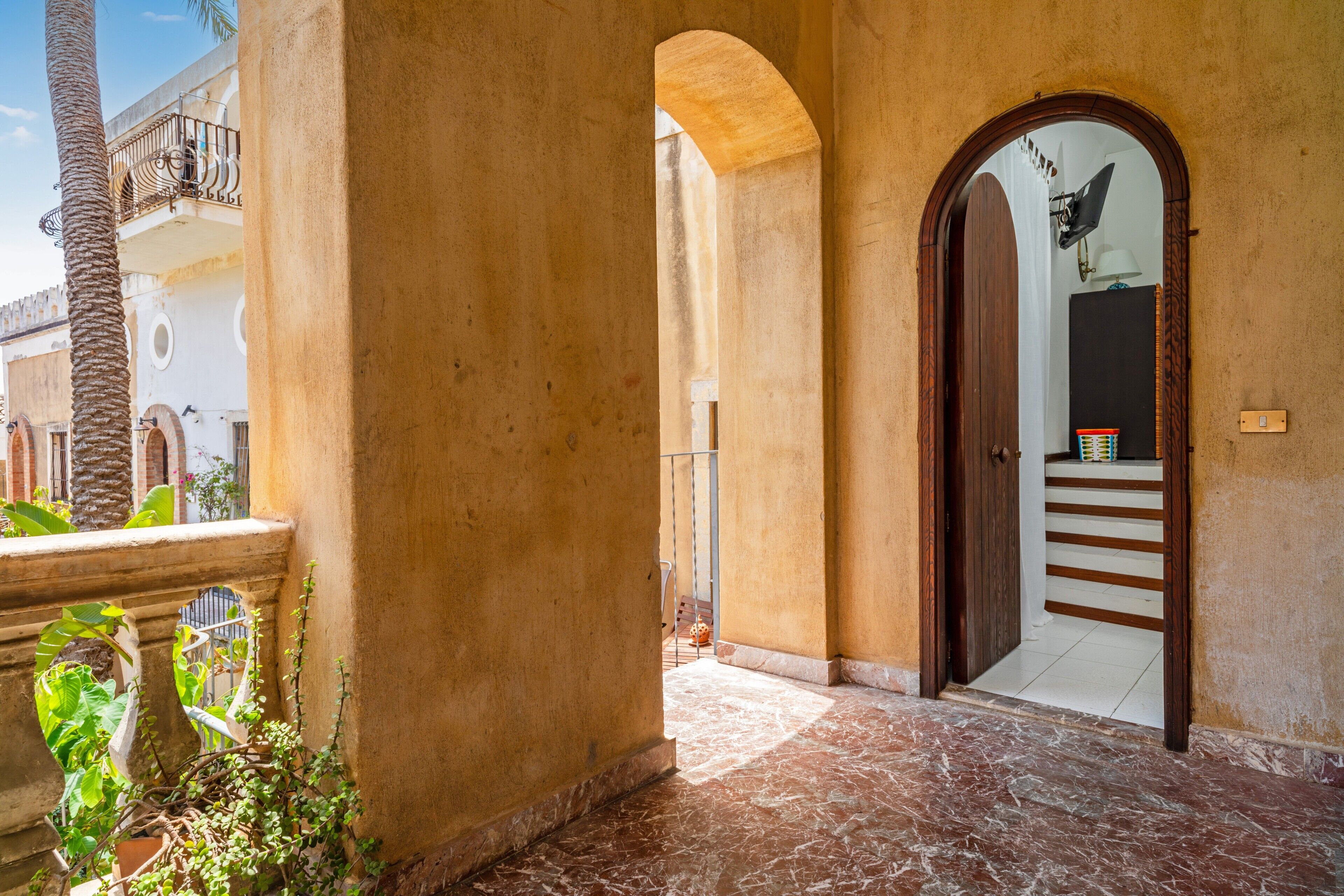 Un corridoio con pavimento in marmo, una porta in legno e un balcone con ringhiera.