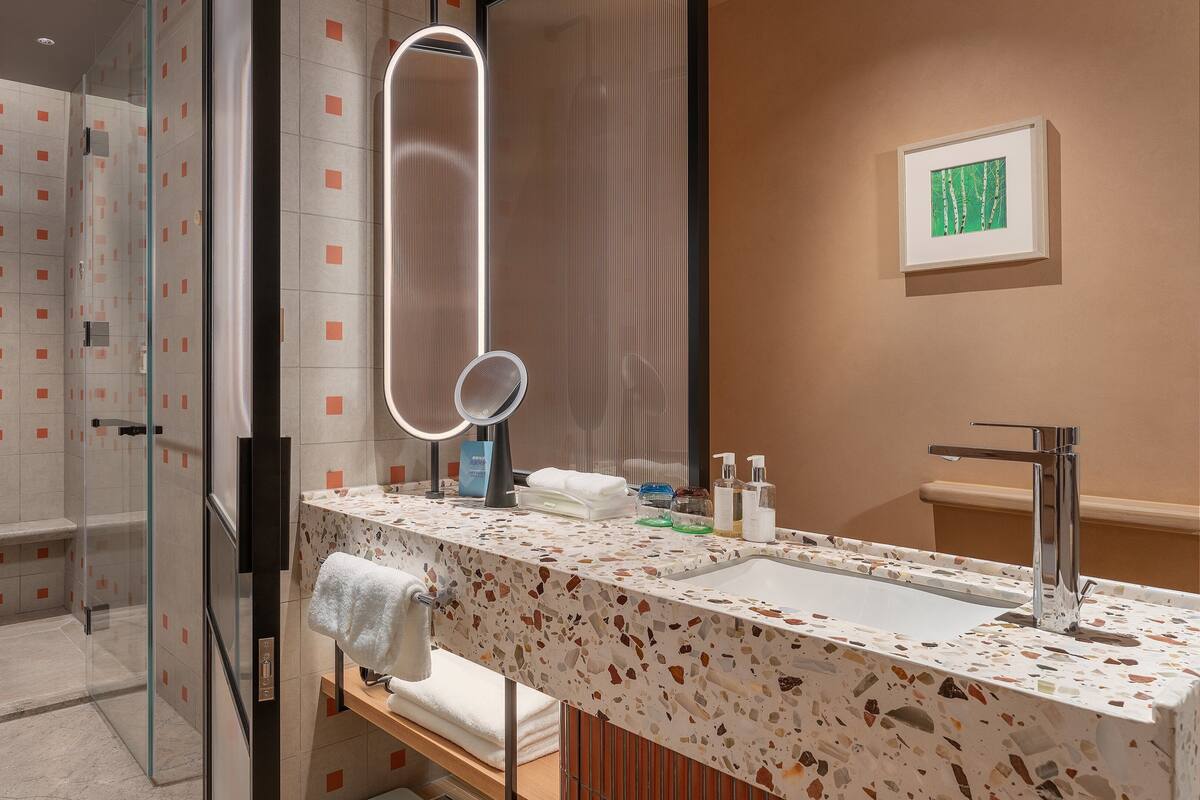 A modern bathroom with a glass shower enclosure, a large mirror, and a vanity with a terrazzo countertop.