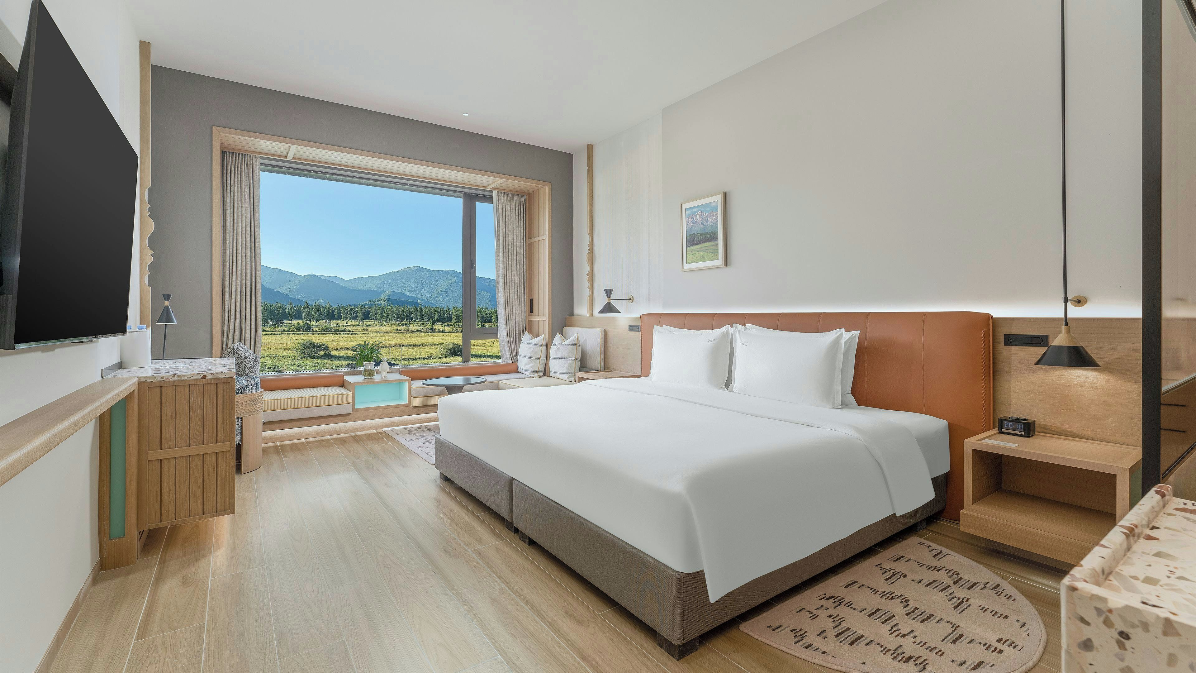 A hotel room with a large bed, a desk, a TV, and a view of mountains.