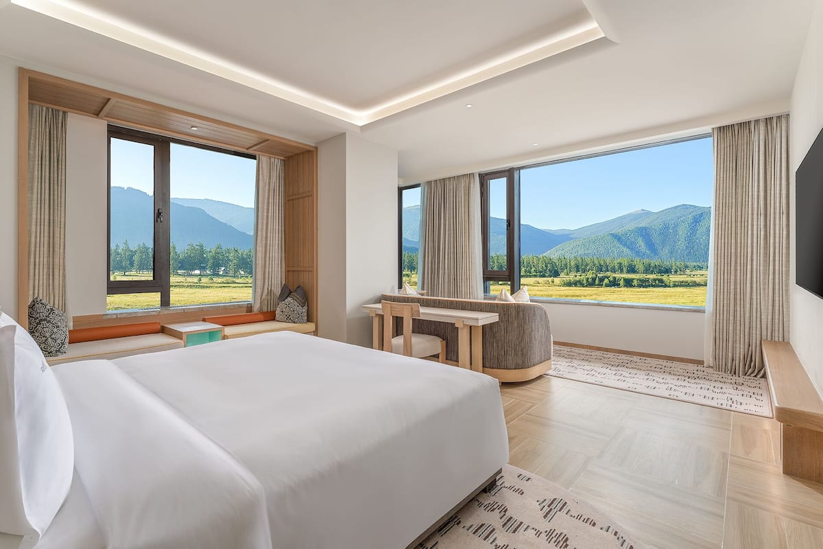 A modern hotel room with a large bed, a desk, and a view of mountains.