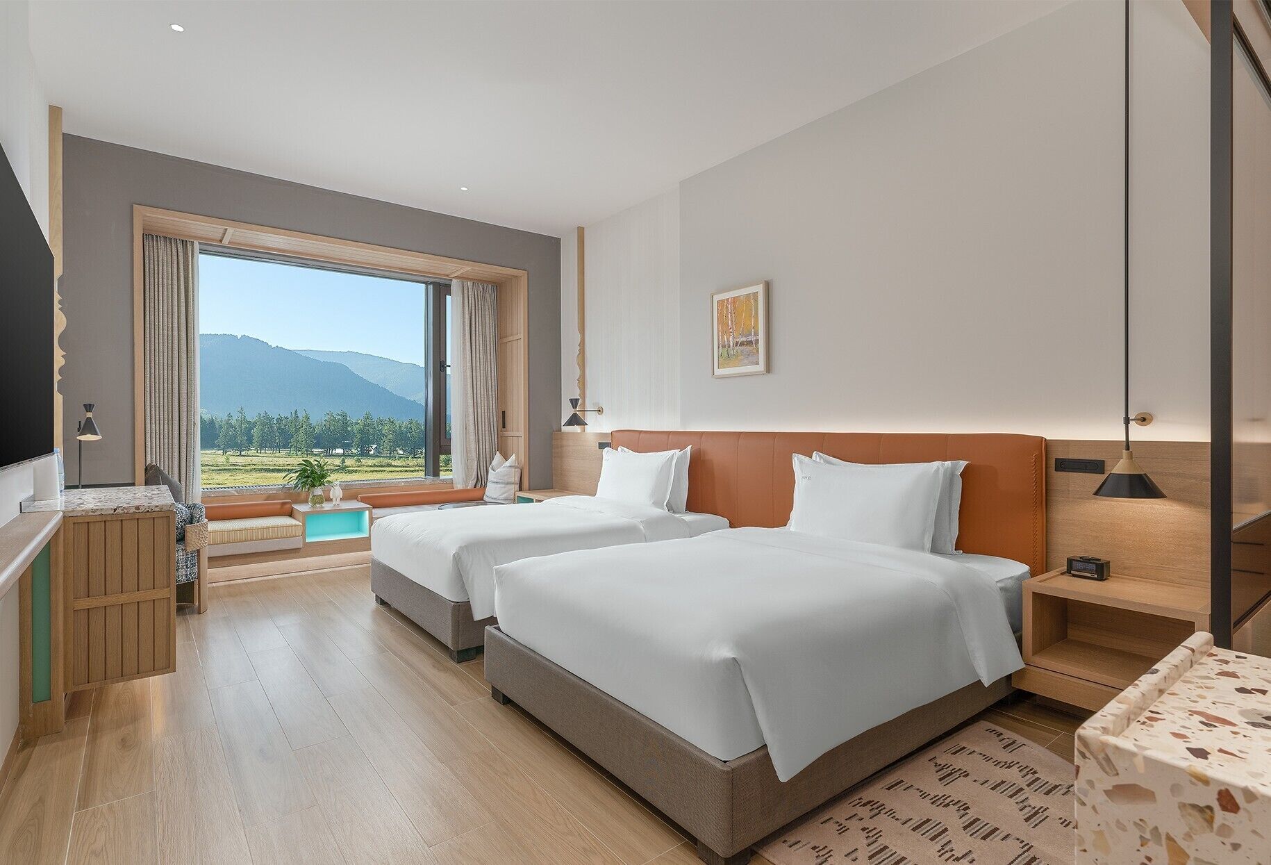 A hotel room with two beds, a large window with a mountain view of mountains, a desk with a lamp, and a small table with a lamp.