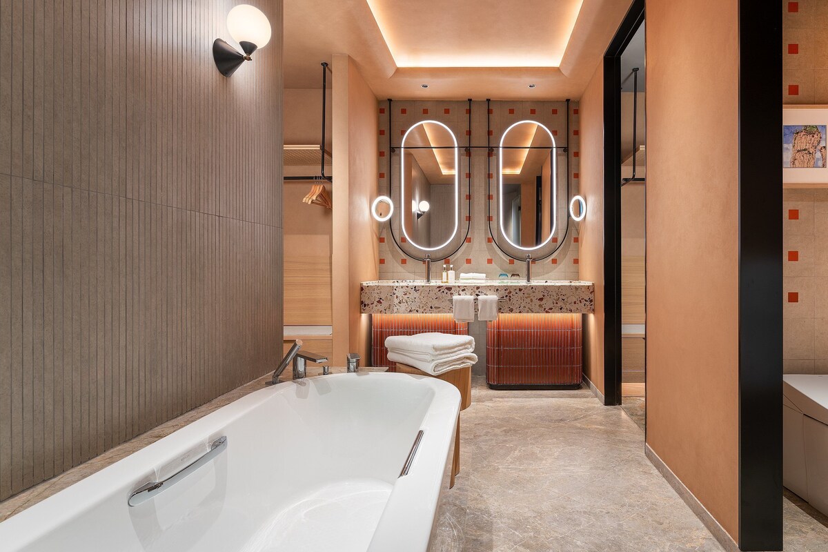 A modern bathroom with a large bathtub, two mirrors, a vanity with a sink, and a toilet.