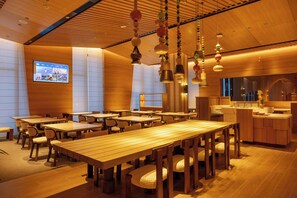 A restaurant interior with wooden tables and chairs, hanging pendant lights, and a projection screen on the wall. - Holiday Inn Resort Kanas Hemu by IHG (Burqin)