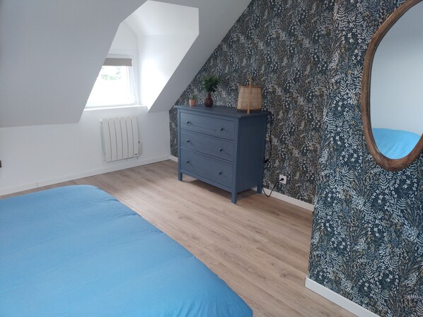 A bedroom with a sloped ceiling, a wooden dresser, a large bed, and a floral wallpaper. - VKLS 3 2-bedroom apartment (Languidic)