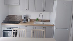 Una cocina compacta con armarios grises, cafetera, lavabo y refrigerador.