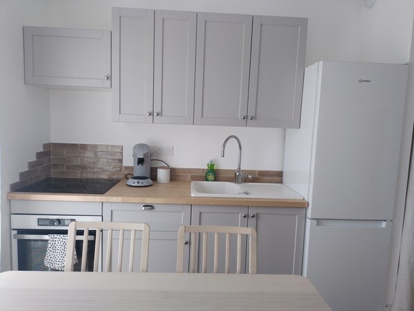 Una cocina compacta con armarios grises, cafetera, lavabo y refrigerador.