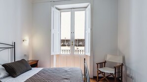 A bedroom with a bed, a chair, a nightstand, and a window with an open door. - Casa Amalfitana by Wonderful Italy (Syracuse)