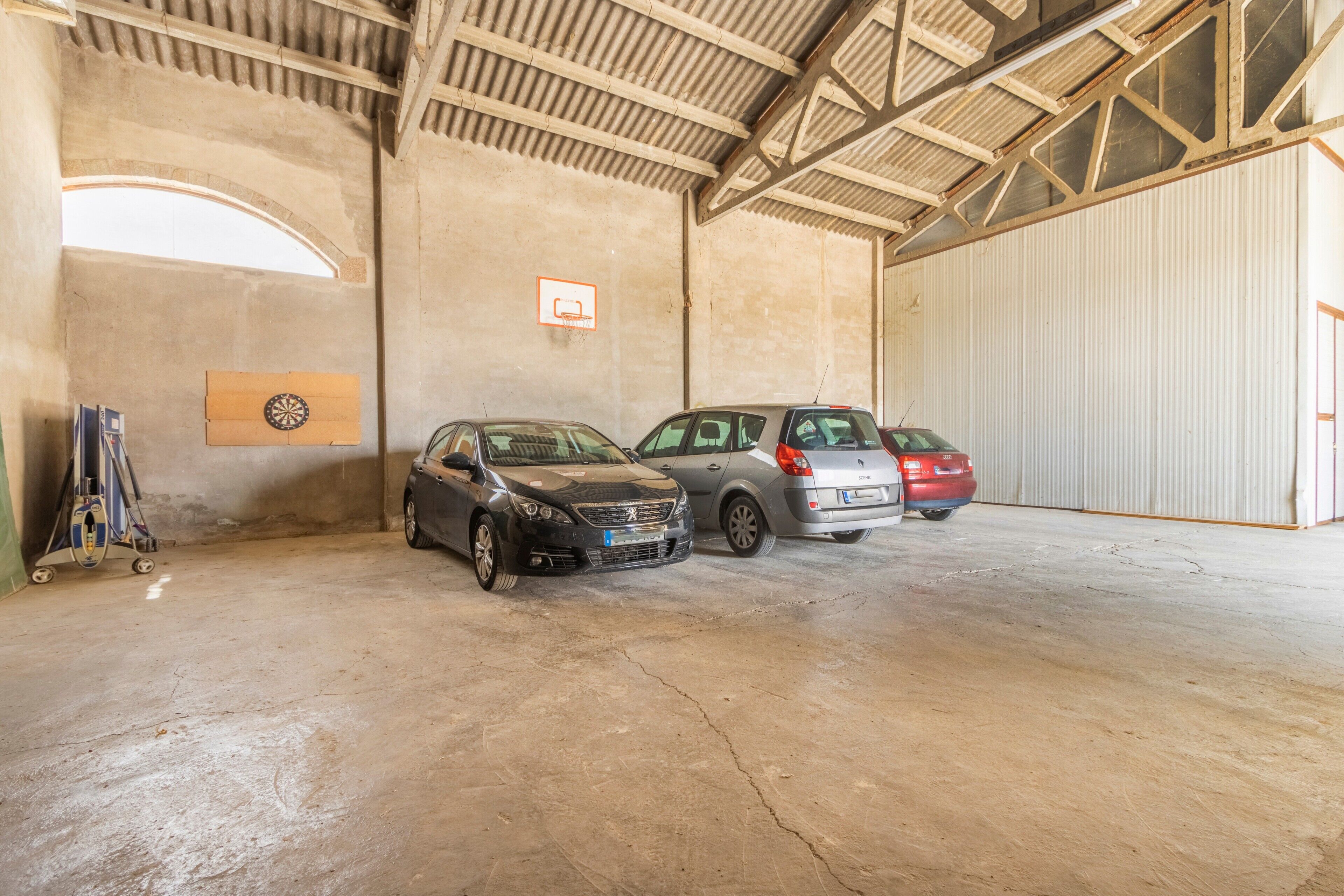 Un vaste espace de stationnement intérieur où sont garées deux voitures, un panneau en bois fixé au mur et une grande porte blanche.