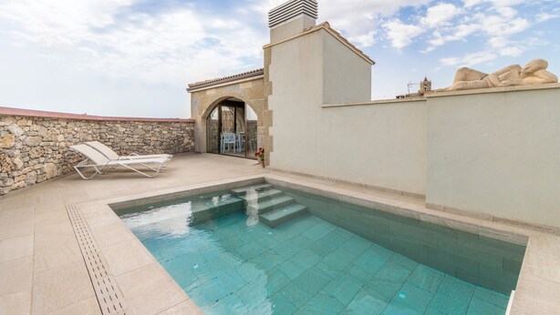 Ein Pool mit Stufen, einer Steinmauer und einer Liegefläche mit Stühlen.