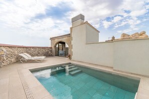Une piscine avec des marches permettant d’y accéder, un mur en pierre et un espace détente avec des fauteuils.