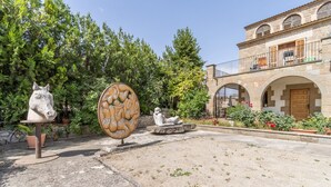Ein Innenhof mit einer Pferde-Skulptur, einem großen runden Stein und einem Gebäude mit Bogenfenstern und einem Balkon.