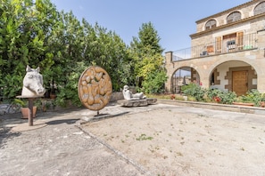 Un patio con una escultura de caballo, una gran piedra circular y un edificio con ventanas de arco y un balcón.