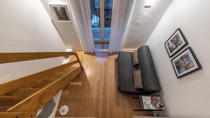 A modern room with a wooden staircase, a grey sofa, and a small shelf with a 'home' sign and decorative items. - Casa Abbanniata a Ballaro' by Wonderful Italy (Palermo)