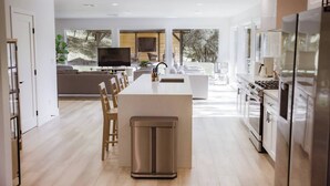 A modern kitchen with a central island, built-in appliances, and a large window offering a view of the outdoors. - Treehouse Overlook at Lakewood (Auburn)