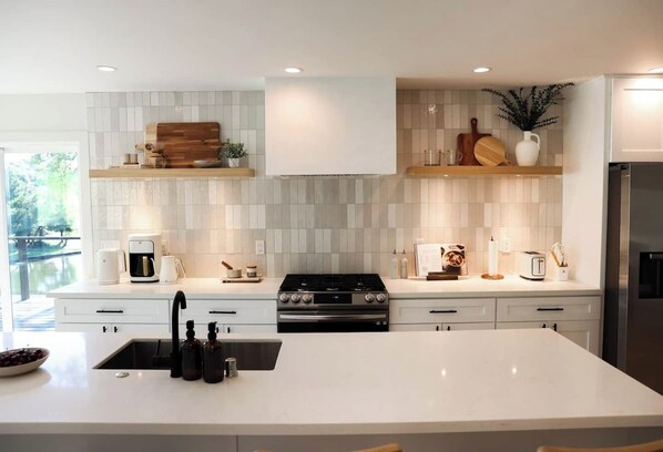 A modern kitchen with a central island, white cabinetry, and a stainless steel refrigerator. - Treehouse Overlook at Lakewood (Auburn)