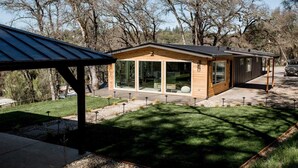 A modern house with large glass windows, a wooden exterior, and a covered patio area. - Treehouse Overlook at Lakewood (Auburn)