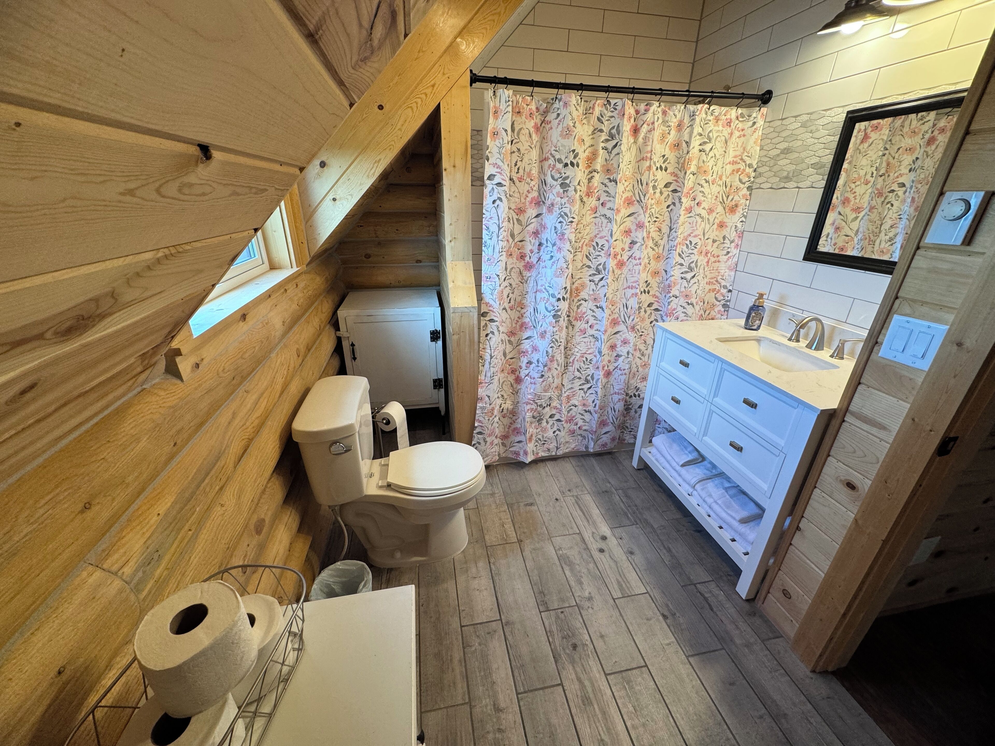 Baño de una cabaña de madera compacta, con inodoro, lavabo y cortina de ducha.
