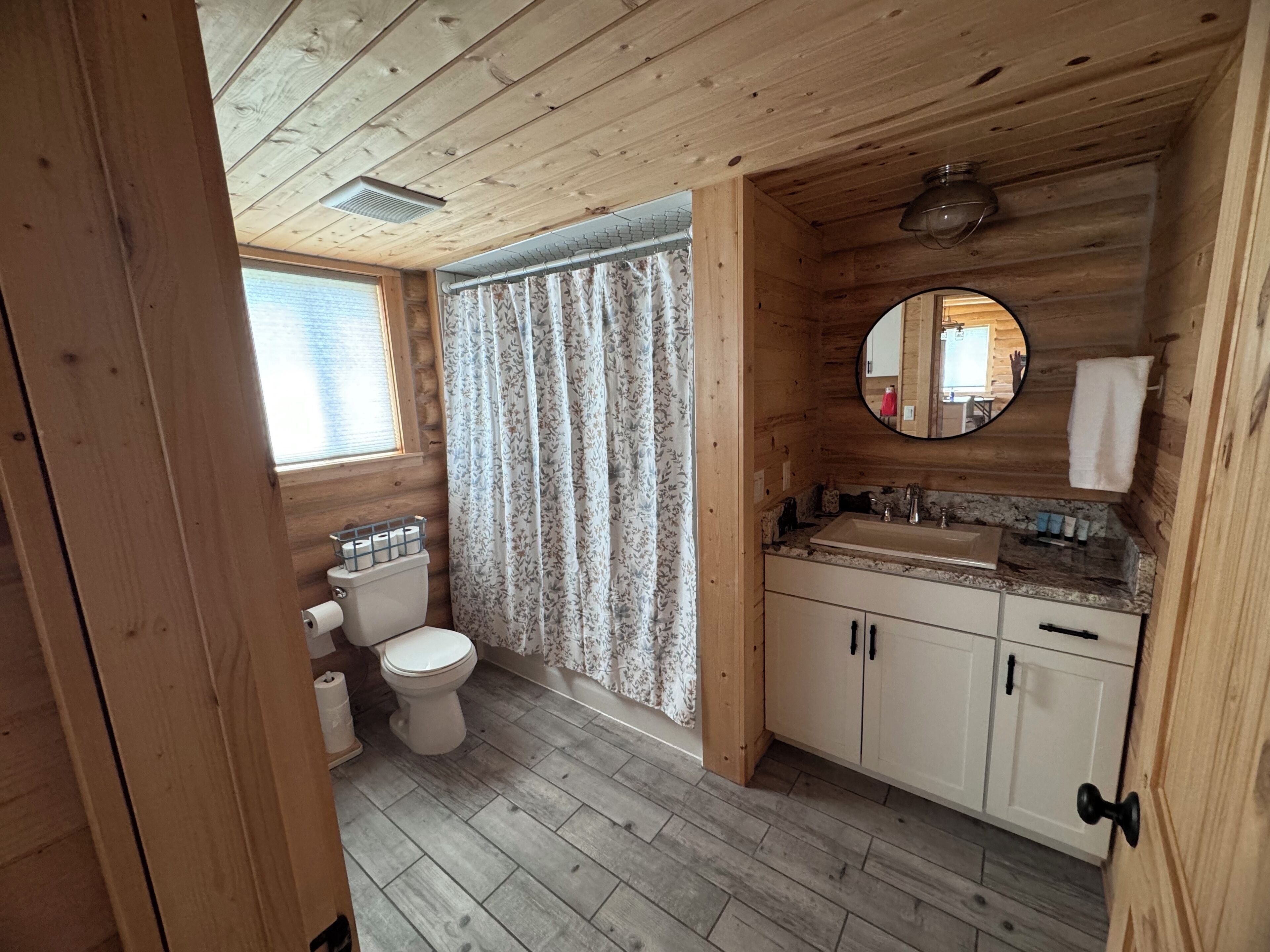 Baño de cabaña de madera con inodoro, lavamanos y cortina de ducha.