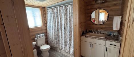 Baño de cabaña de madera con inodoro, lavamanos y cortina de ducha.