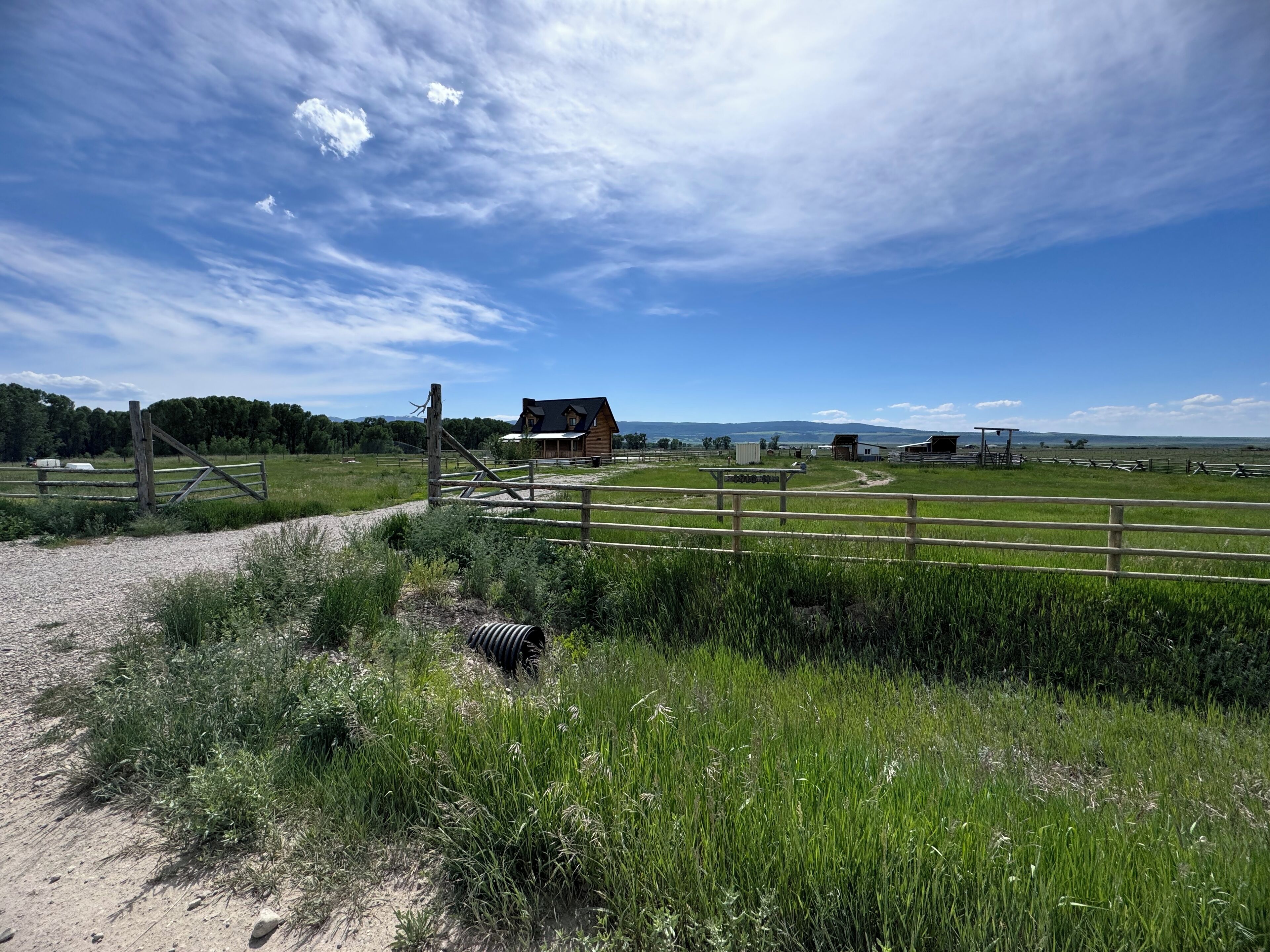 A rural landscape with a wooden fence, a gravel path, and a house in the background.