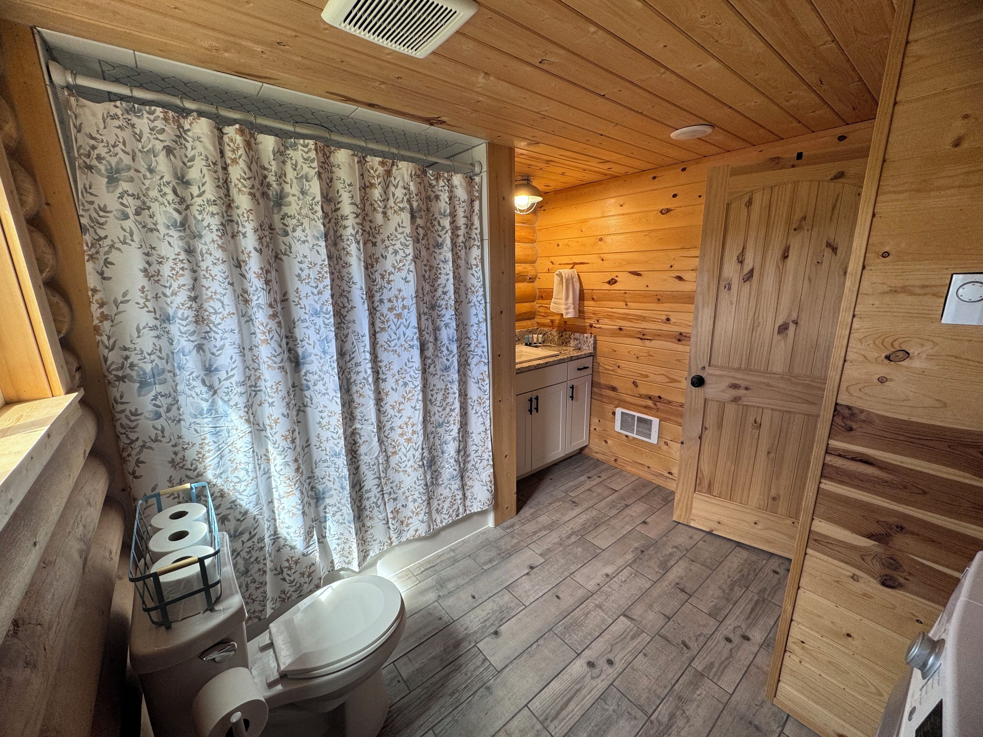 A wooden cabin bathroom with a toilet, shower curtain, and wooden walls.