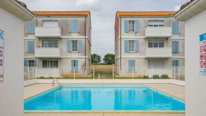 Ein Swimmingpool mit weißem Zaun, umgeben von Gebäuden mit Balkonen und blauen Fensterläden.