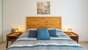 Ein Bett mit gestreifter Bettdecke, zwei Kissen, ein Holzkopfbrett, zwei Nachttische mit Lampen und ein Wandbild.