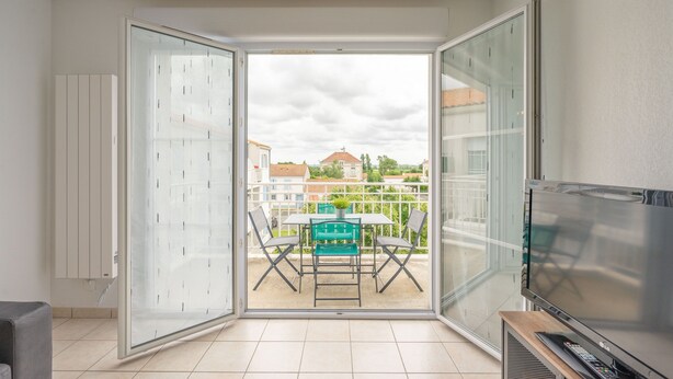 Ein offener Balkon mit Tisch und Stühlen, einem Fernseher und Blick auf Gebäude.