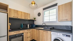 Eine moderne Küche mit Holzschränken, einem Einbauofen, einer Waschmaschine und einem Fenster mit Jalousien.