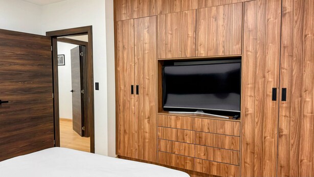 Quarto com cama, guarda-roupa de madeira e televisão na parede.
