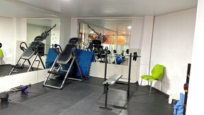 Academia com equipamentos de ginástica, espelho e uma cadeira azul.