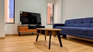 Uma sala de estar moderna com uma mesa de centro de madeira, um sofá azul e uma TV de tela plana em um armário de madeira.