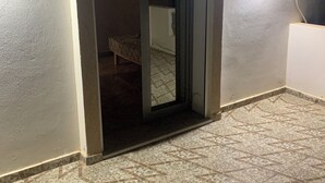 A room with a tiled floor, a doorway leading to another room, and a wall-mounted light fixture. - Maison (Médenine)