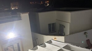 A rooftop terrace with a covered table and chairs, a small round table, and a person using a smartphone. - Maison (Médenine)