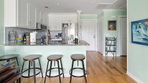 Una cocina moderna con armarios blancos, un refrigerador de acero inoxidable y una barra con taburetes.