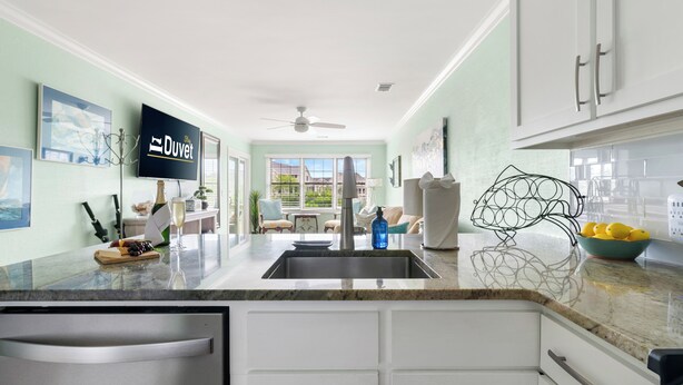 Una cocina moderna con armarios blancos, un lavamanos de acero inoxidable y un ventanal amplio.