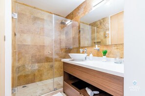 A modern bathroom with a glass-enclosed shower, a white sink, and a wooden vanity.
