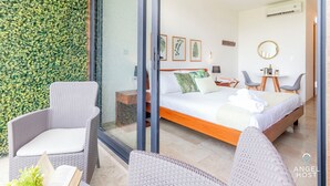 Habitació d'hotel moderna amb un llit gran, dues cadires, una taula petita i vistes a una paret verda.
