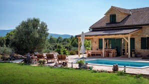 Une maison en pierre avec une piscine, un espace salon extérieur et une vue sur les montagnes.