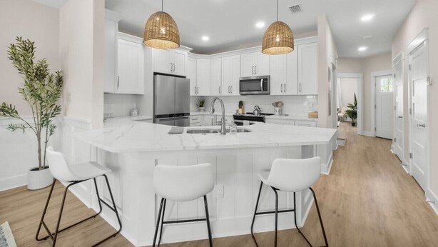 Uma cozinha moderna com armários brancos, uma ilha central com banquetas e duas luminárias pendentes de vime.