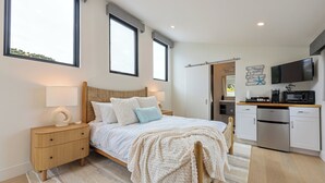 Un dormitorio con cama, mesitas de noche, un televisor y una cocina equipada con microondas y refrigerador.
