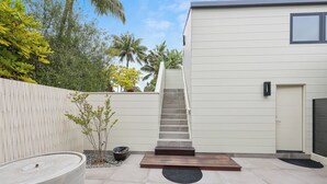 Un patio exterior moderno con una fuente de agua de hormigón, un banco de madera y una escalera que lleva a una puerta.